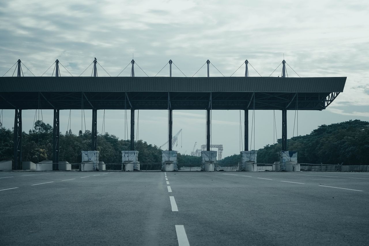 Empty multi-lane roadway passing beneath a large canopy with concrete barriers positioned across the lanes.