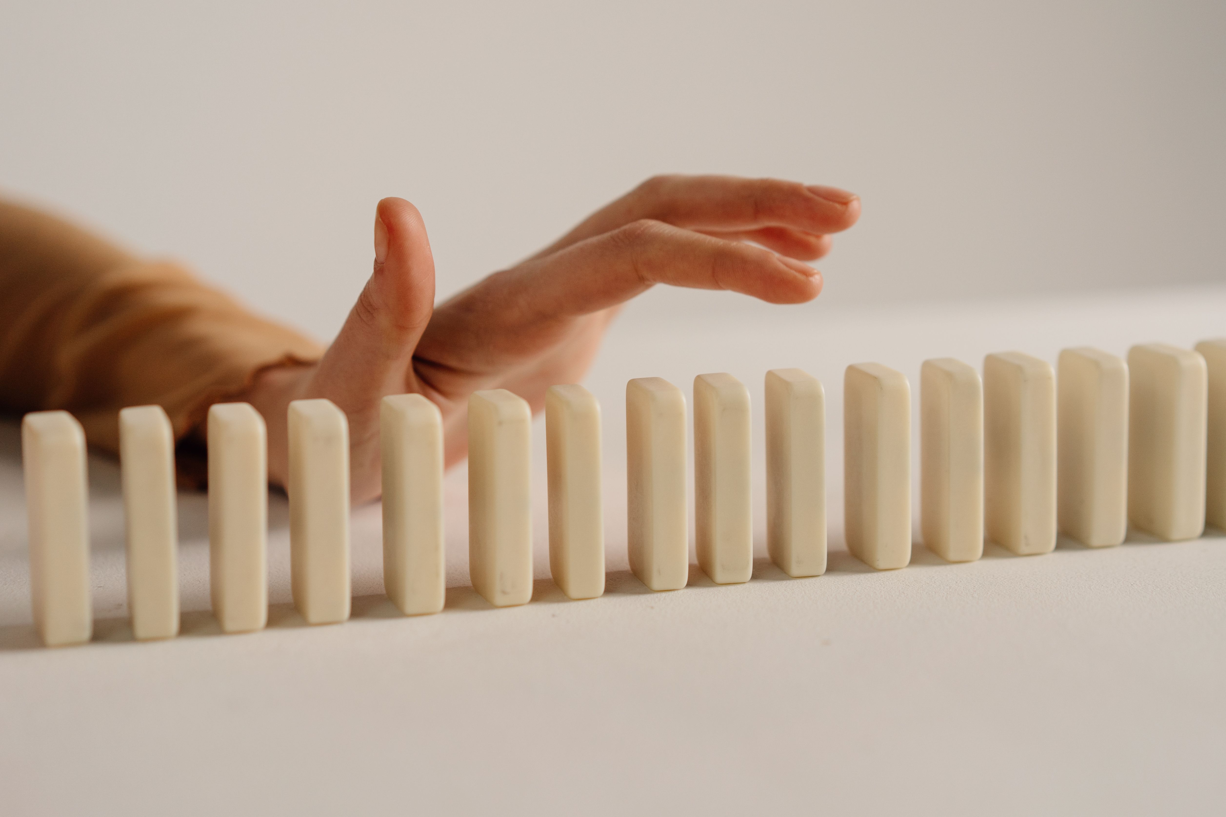 A hand reaching over a row of upright white dominoes arranged closely together.