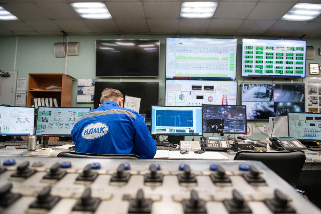 Operator seated in an industrial control room surrounded by monitoring screens and control panels.